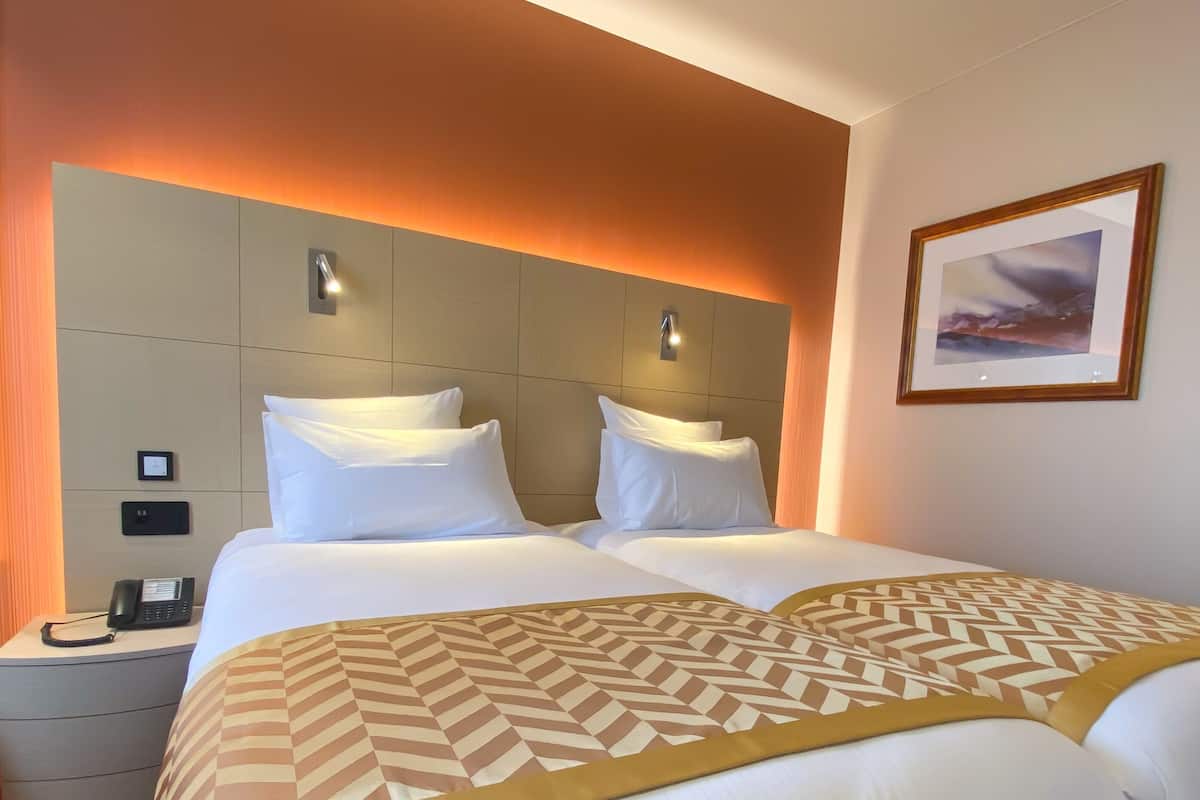 Hotellihuone, jossa on suuri sänky, kaksi yöpöytää, puhelin ja seinällä oleva kehystetty kuva.