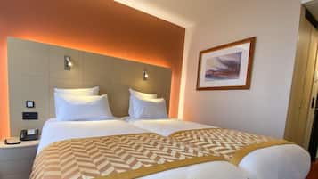 Habitación de hotel con una cama grande, dos mesitas de noche, un teléfono y un cuadro en la pared.