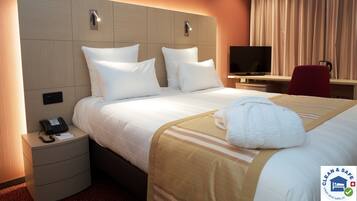 A hotel room with a bed, bedside table with a phone, a TV, and a desk with a chair.