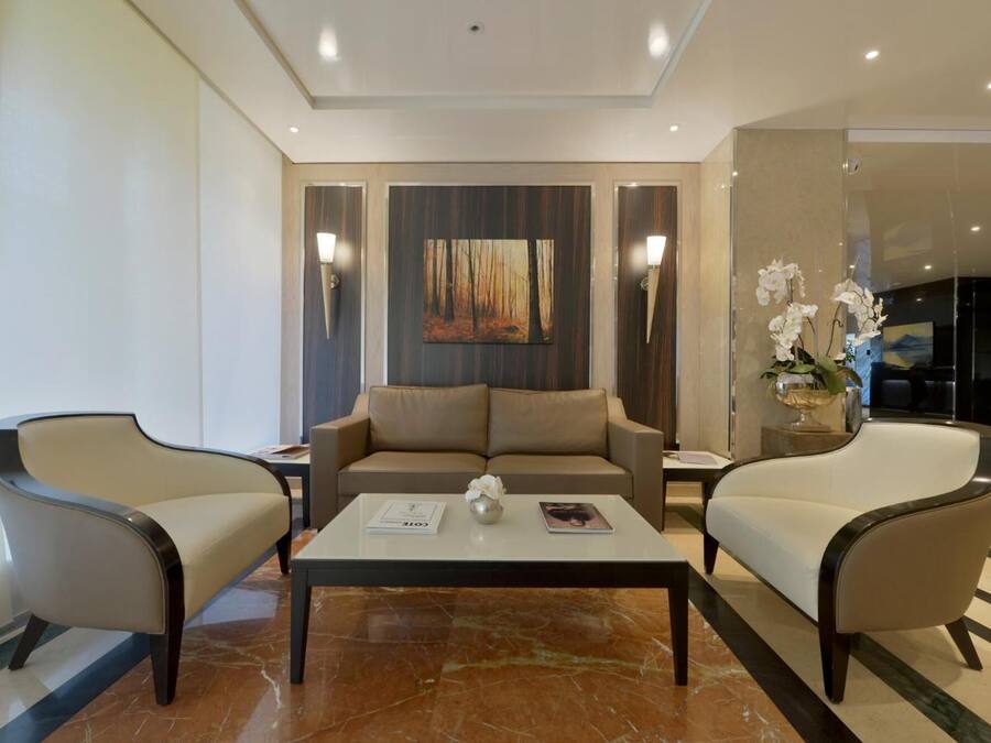 A modern hotel lobby with a sofa set, two armchairs, a coffee table, and a painting on the wall.