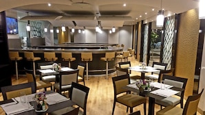 Un restaurante moderno con varias mesas y sillas, una zona de bar y una cocina al fondo.