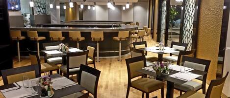 Un restaurante moderno con varias mesas y sillas, una zona de bar y una cocina al fondo.