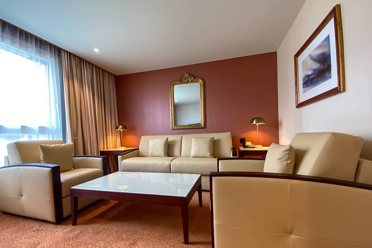 Hotellihuoneessa on beigenvärinen sohvaryhmä, lasinen sohvapöytä ja suuri peili seinällä.