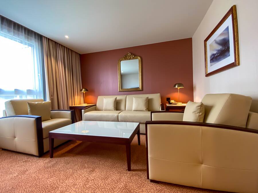Habitación de hotel con sofá color beige, una mesa de centro de vidrio y un espejo grande en la pared.