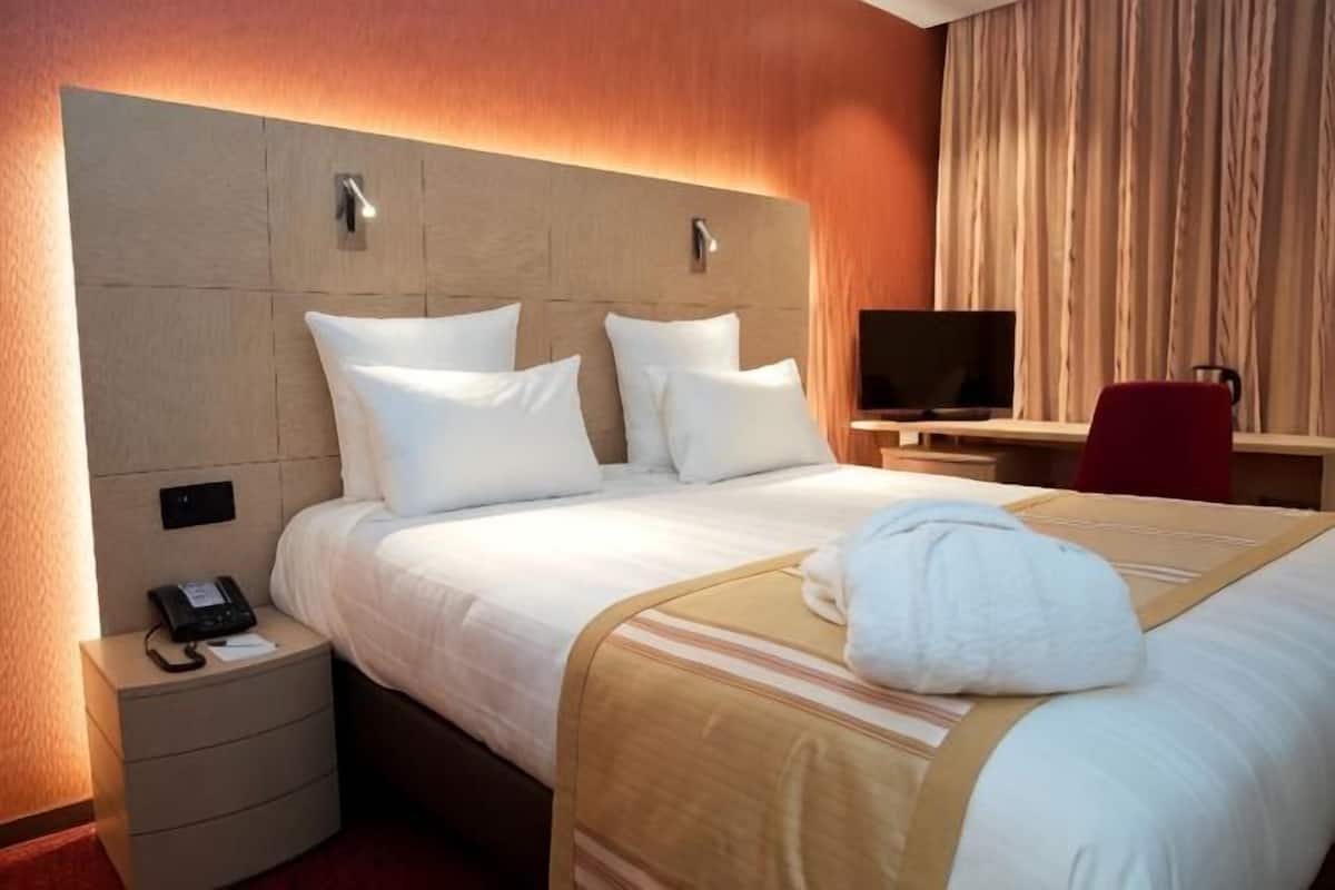 Hotellihuone, jossa on sänky, yöpöytä puhelimella, televisio ja tuoli.