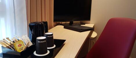 Habitación de hotel con escritorio, una silla roja, televisor y una bandeja con tazas de café y cafetera.