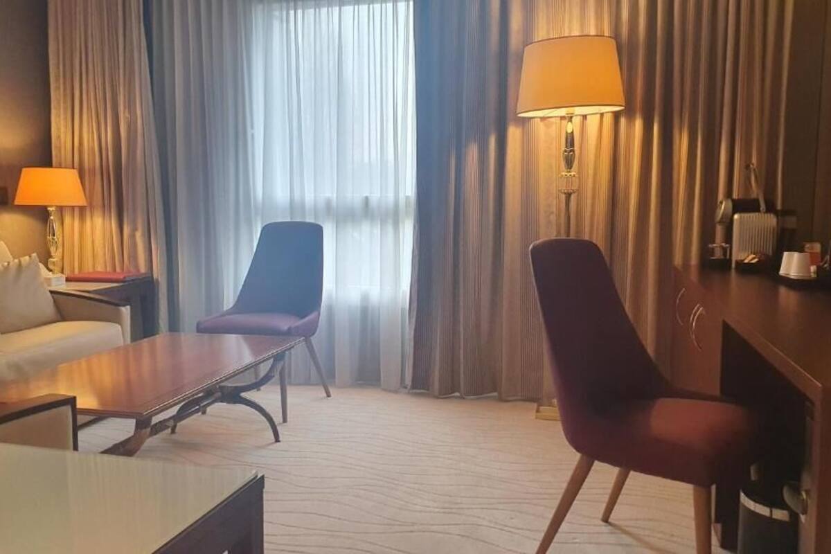 Hotellihuone, jossa on sohva, tuoli, sohvapöytä, lamppu ja patteri.