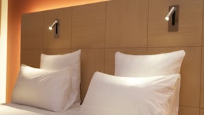 Habitación de hotel con cabecera de madera, dos almohadas blancas y cama con ropa de cama blanca.