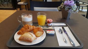 Uma bandeja de café da manhã com croissants, uma xícara de café, um copo de suco de laranja e um pequeno pote de manteiga.