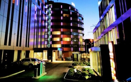 A modern building with a curved facade, multiple balconies, and a parking area in the foreground.
