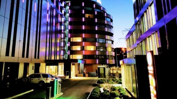 Un edificio moderno con fachada curva, varios balcones y un área de estacionamiento al frente.