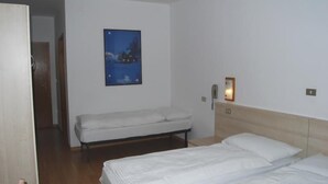 A hotel room with a single bed, a smaller bed, a nightstand, a bedside table, a wall-mounted phone, and a framed picture of a snowy landscape. - Monreal (San Michele All'adige)