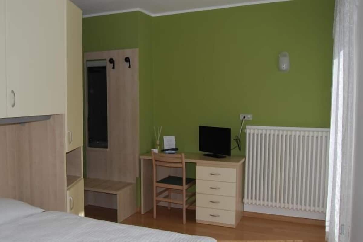Un dormitorio con una cama, un escritorio con una computadora, una silla y un radiador.