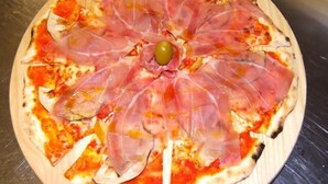 A pizza with prosciutto and an olive on a wooden board. - Monreal (San Michele All'adige)