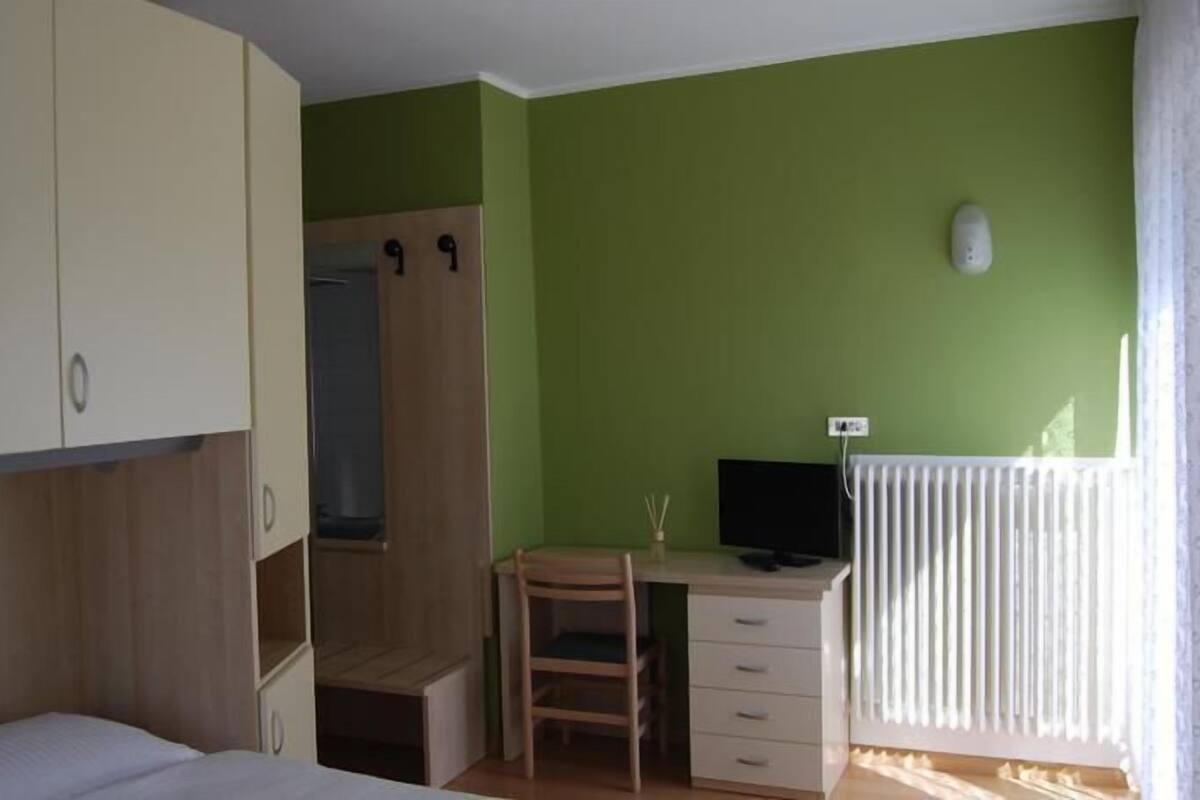 Una habitación con una cama, un escritorio con silla, un armario y un radiador.