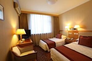 Ein Hotelzimmer mit zwei Betten, einem Schreibtisch mit Lampe, einem Fernseher und einem Telefon.