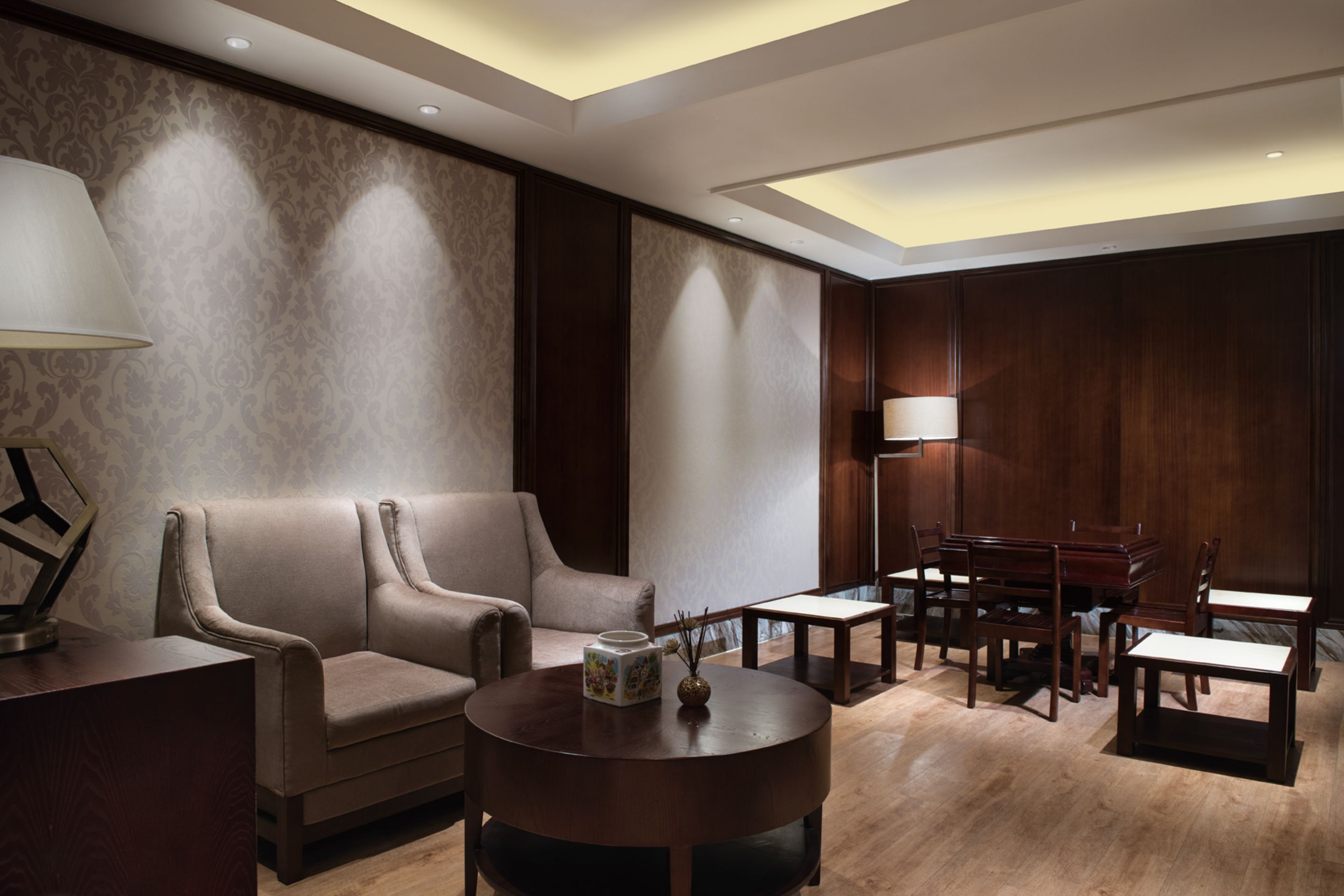 A modern hotel room with a sofa, dining table, chairs, and a lamp.