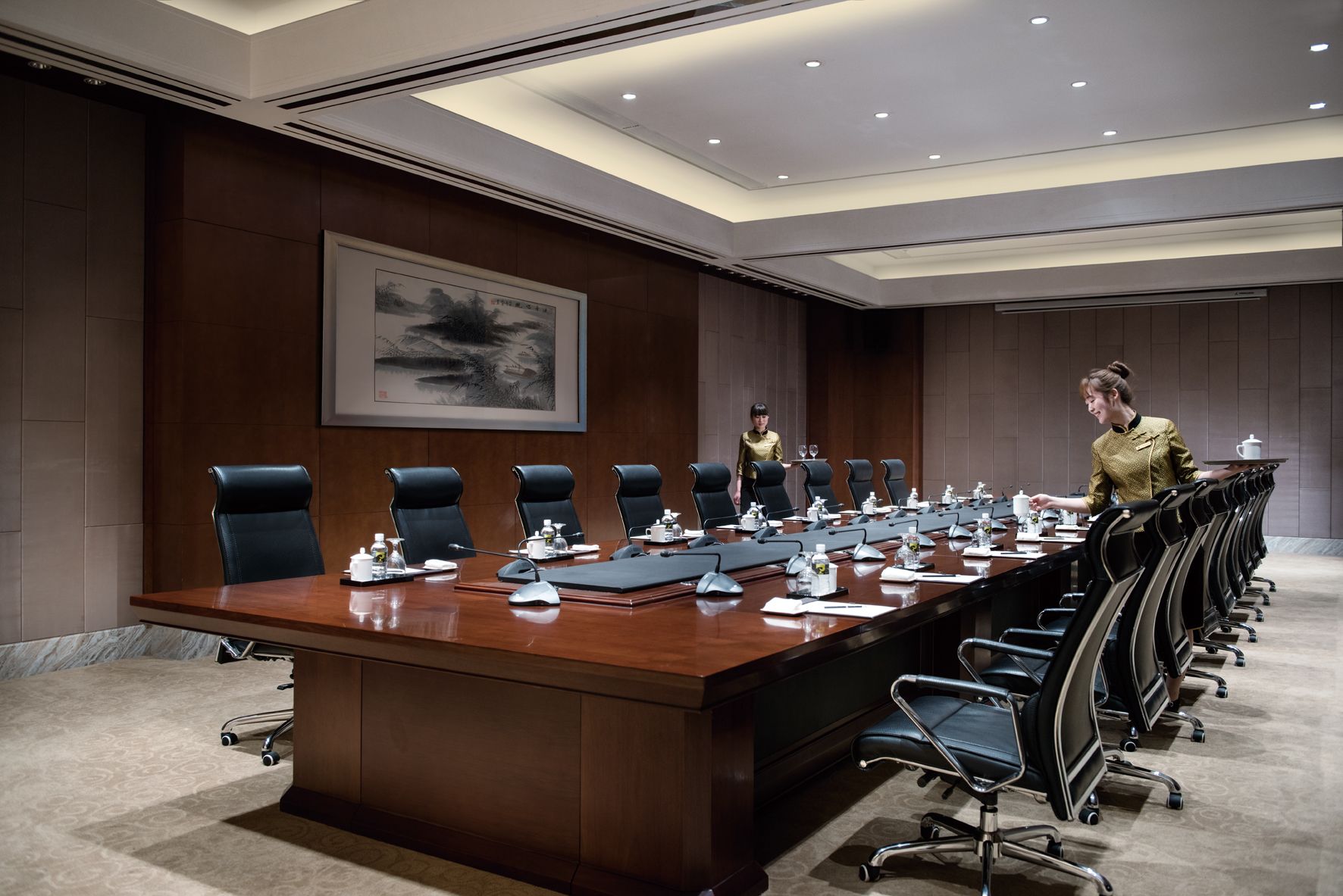 A conference room with a long table, multiple chairs, and a person serving tea.