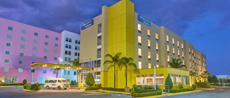 A hotel with a modern design, featuring a yellow and white facade, a covered entrance, and a parking lot.