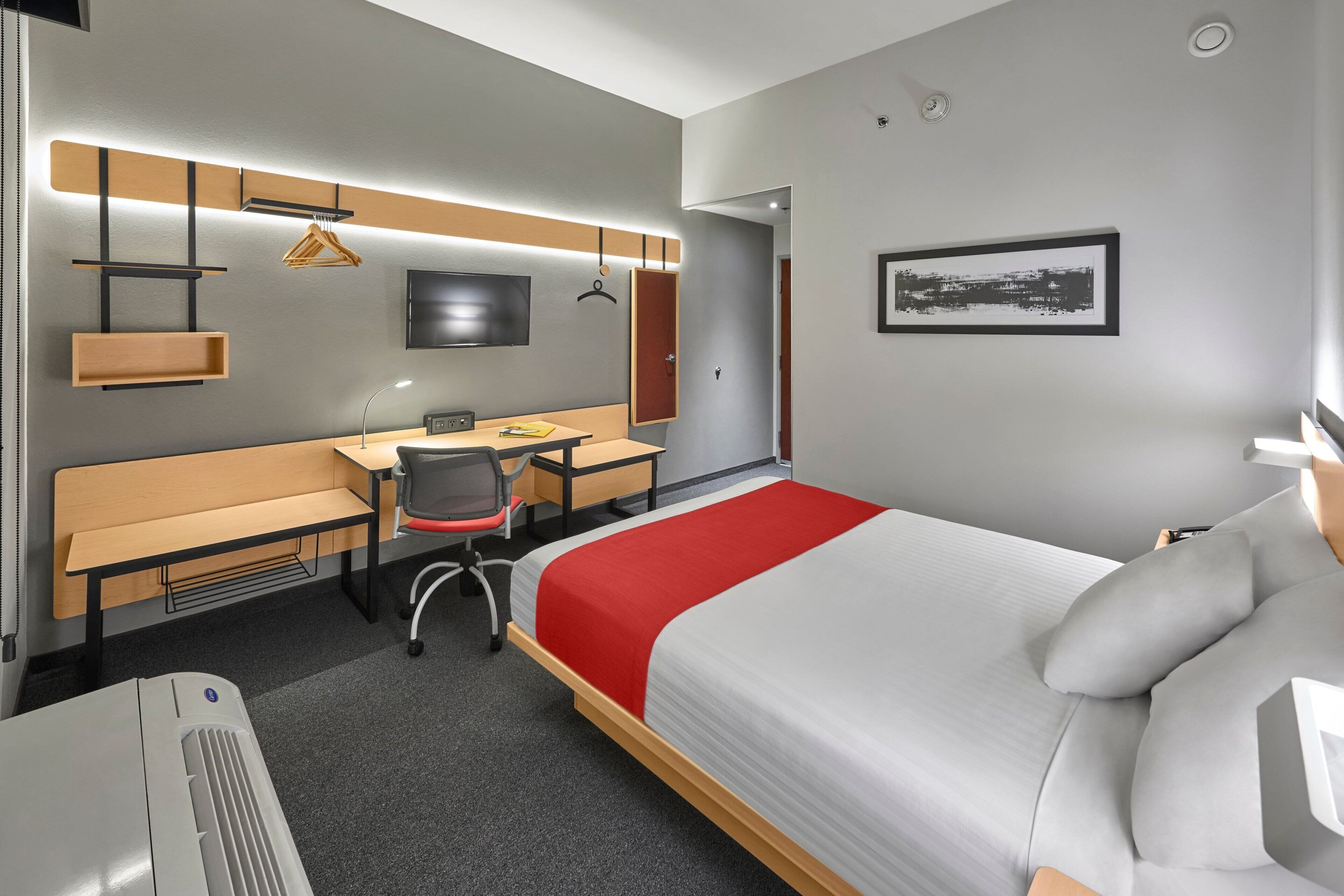 Moderni hotellihuone, jossa on sänky, työpöytä, tuoli ja televisio.