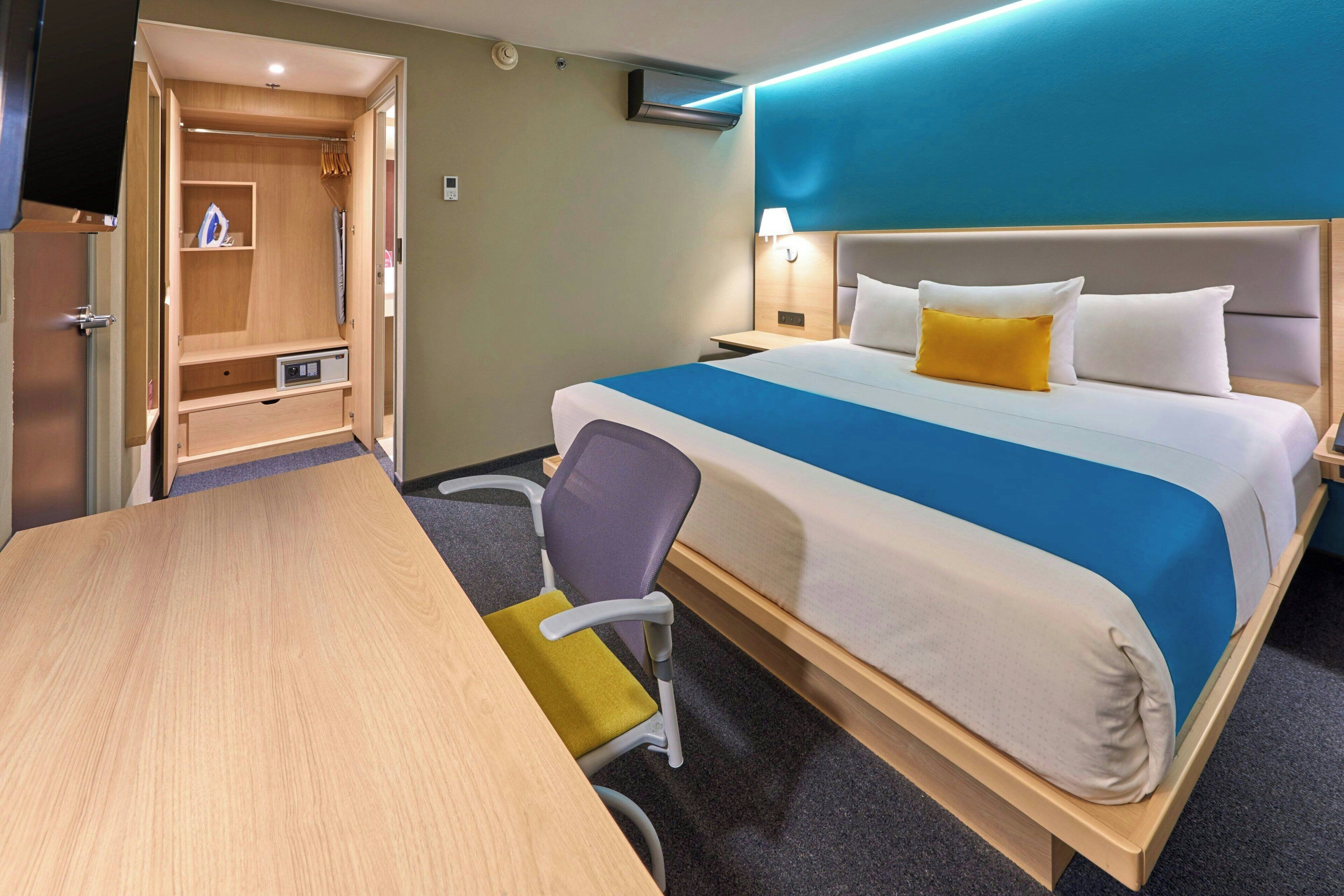 A hotel room with a bed, bedside table, lamp, chair, and a desk.