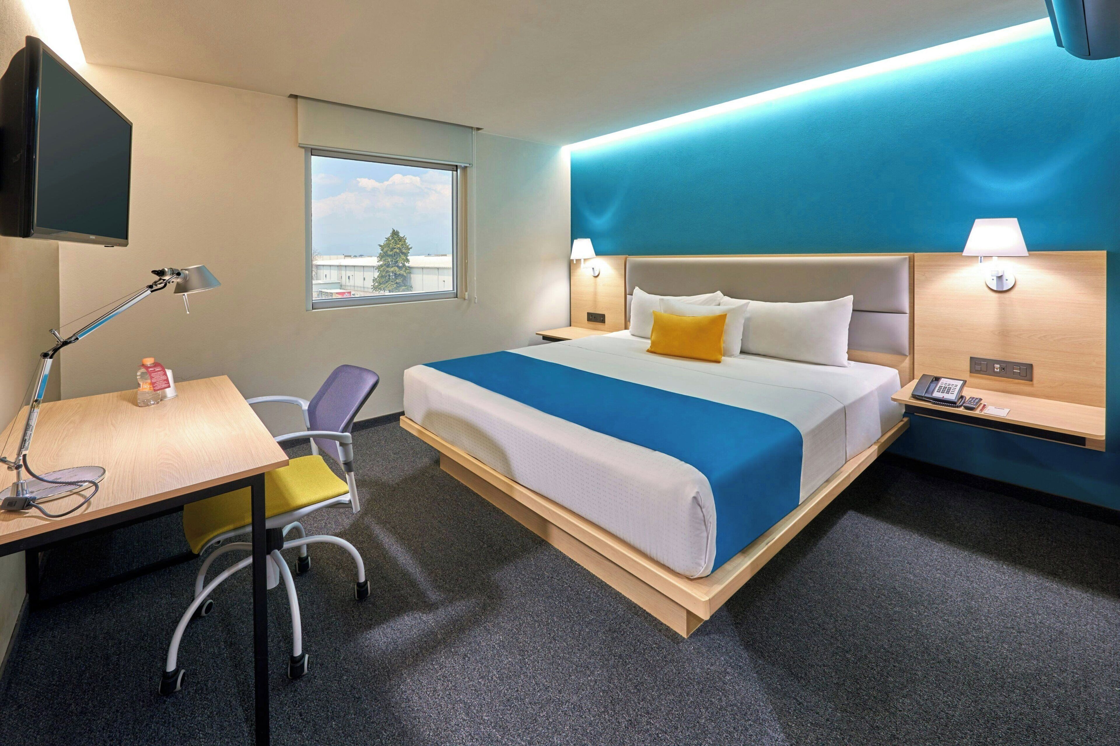 Habitación de hotel con cama, escritorio, silla y ventana.
