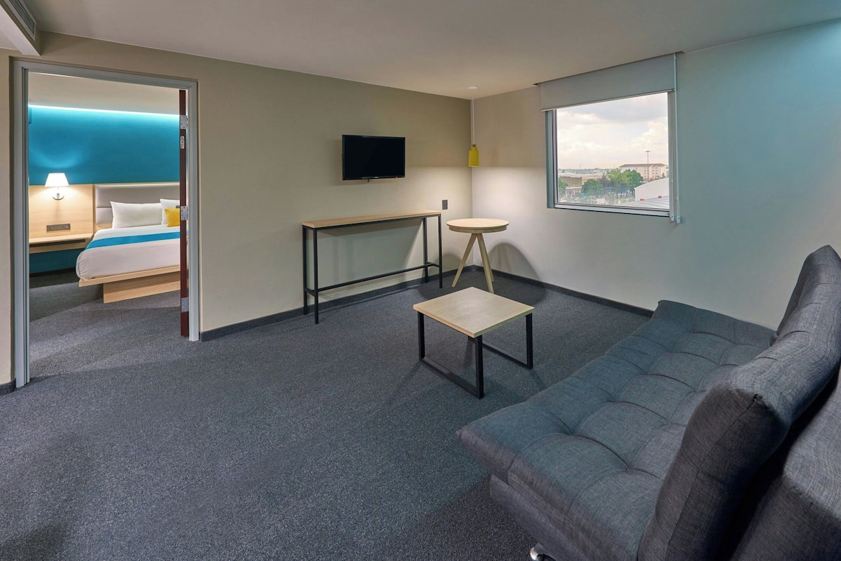 Une chambre d’hôtel avec un lit, une télévision, une petite table, un canapé et une fenêtre donnant sur un beau paysage.