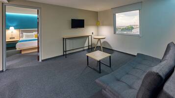 Quarto de hotel com cama, televisão, mesa pequena, sofá e janela com vista.