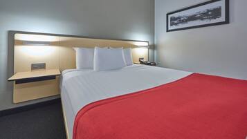 Et hotelværelse med en seng, et sengebord og et billede i ramme på væggen.