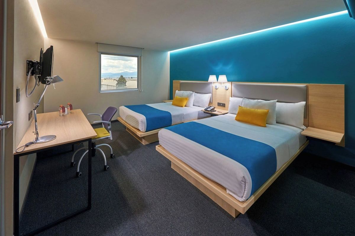 Une chambre d’hôtel avec deux lits, un bureau avec un ordinateur, une chaise et une fenêtre donnant sur un beau paysage.