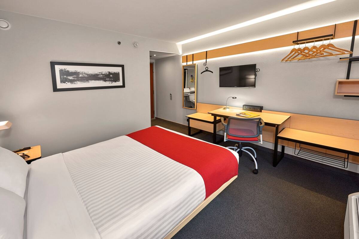 Une chambre d’hôtel avec un lit, un bureau, une chaise et un miroir.