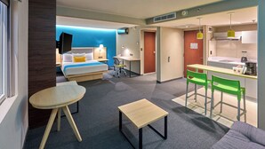 A modern hotel room with a bed, a desk, a chair, a small table, and a kitchenette. - City Express by Marriott Toluca (Toluca)
