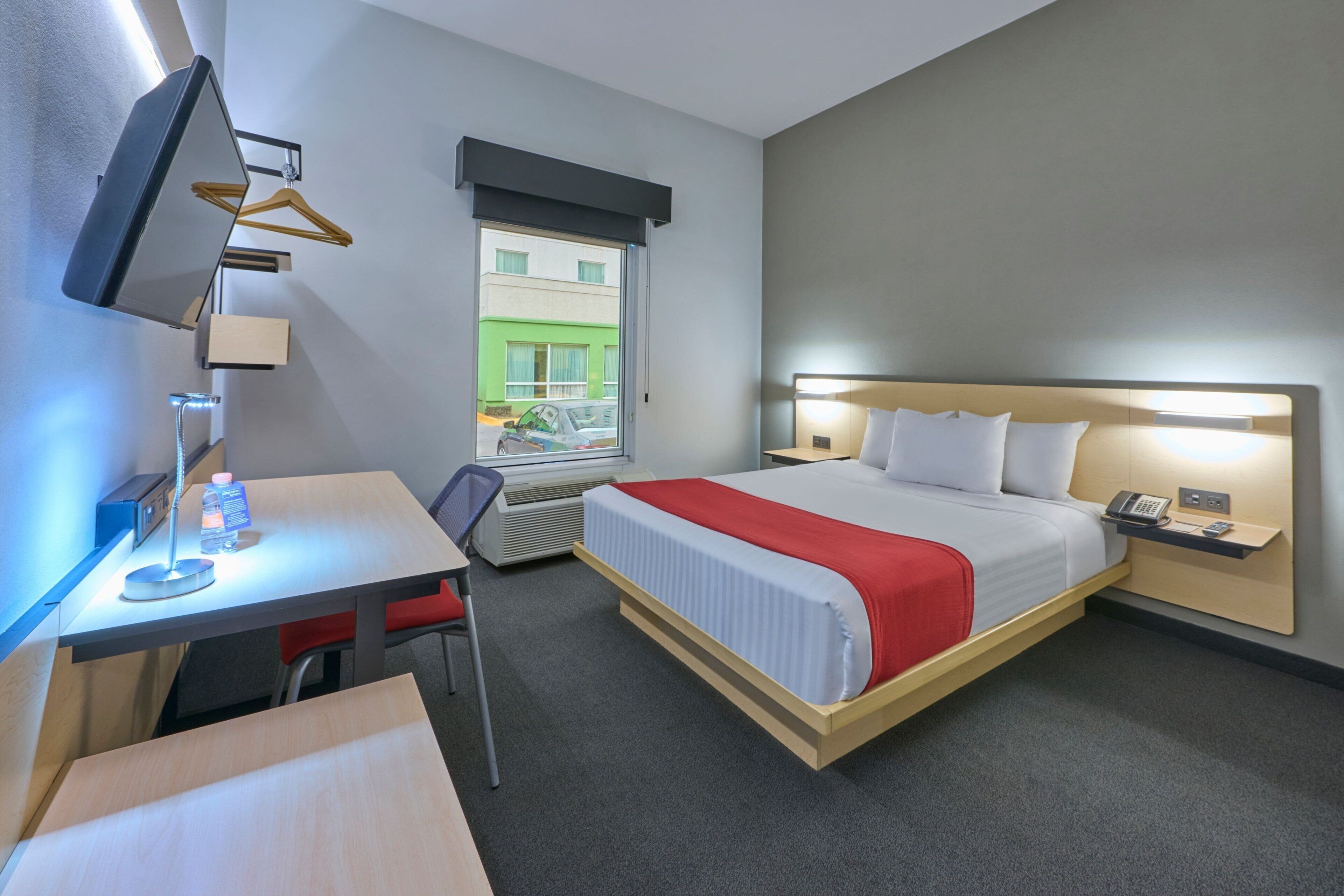 Habitación de hotel con cama, mesita de noche, escritorio, silla y televisión montada en la pared.