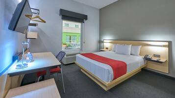 Habitación de hotel con cama, mesita de noche, escritorio, silla y televisión montada en la pared.