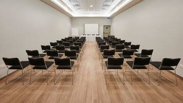 Une salle de conférence avec des rangées de chaises noires disposées face à un tableau blanc situé au fond de la pièce.