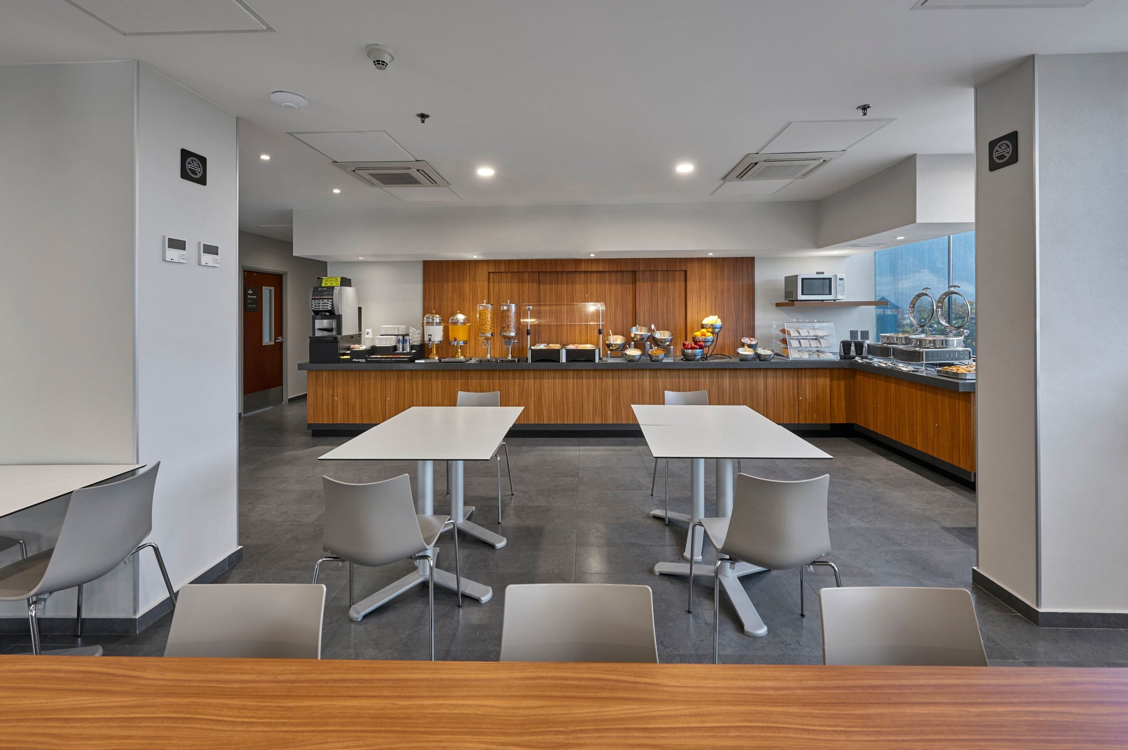 A modern hotel dining area with a central buffet, white tables, and grey chairs.