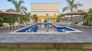 A swimming pool with lounge chairs and umbrellas, surrounded by palm trees and a building in the background. - City Express by Marriott Tampico (Tampico)