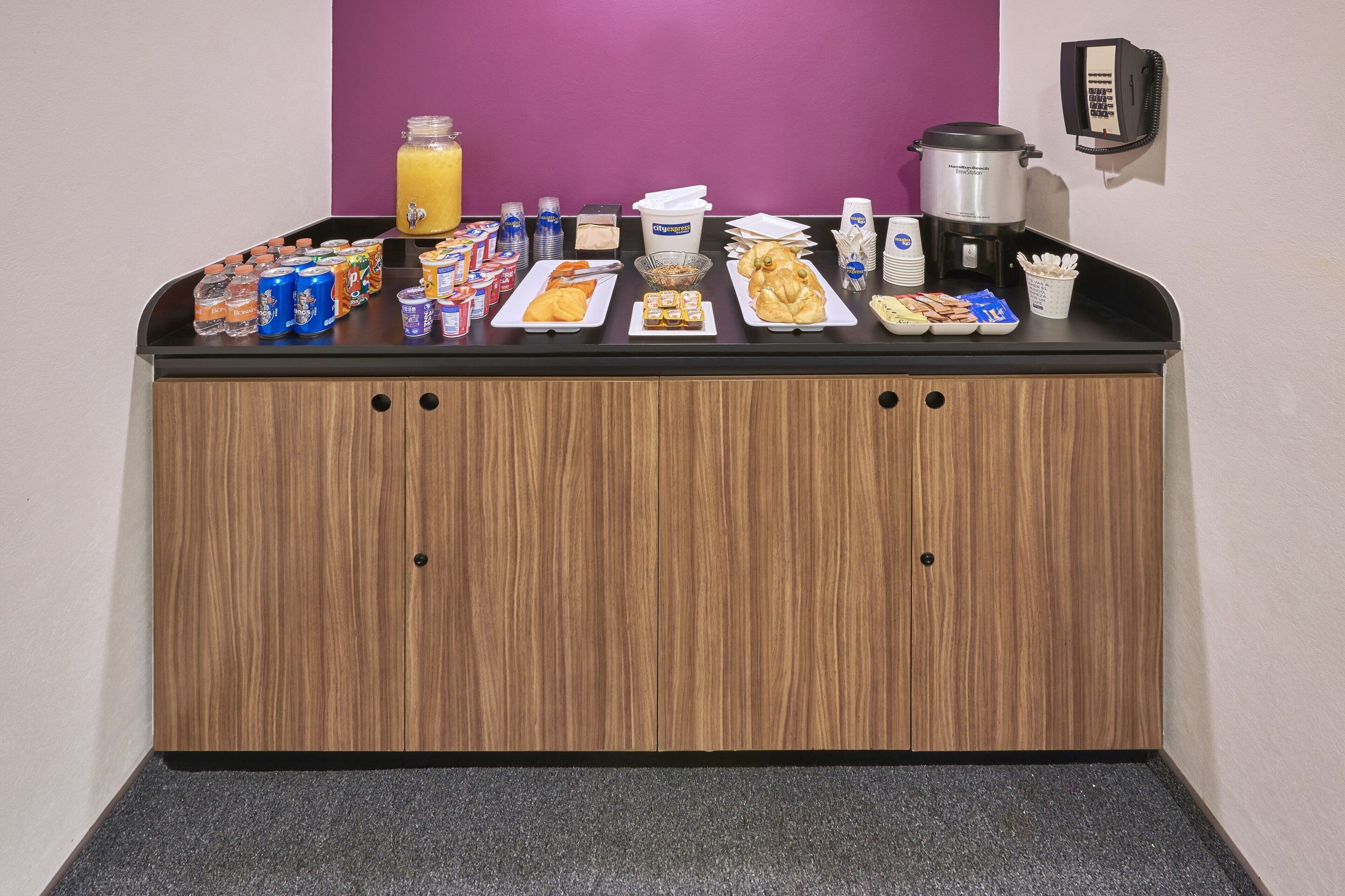 Una barra de desayuno con diversas opciones de comida, bebidas y una máquina de café.