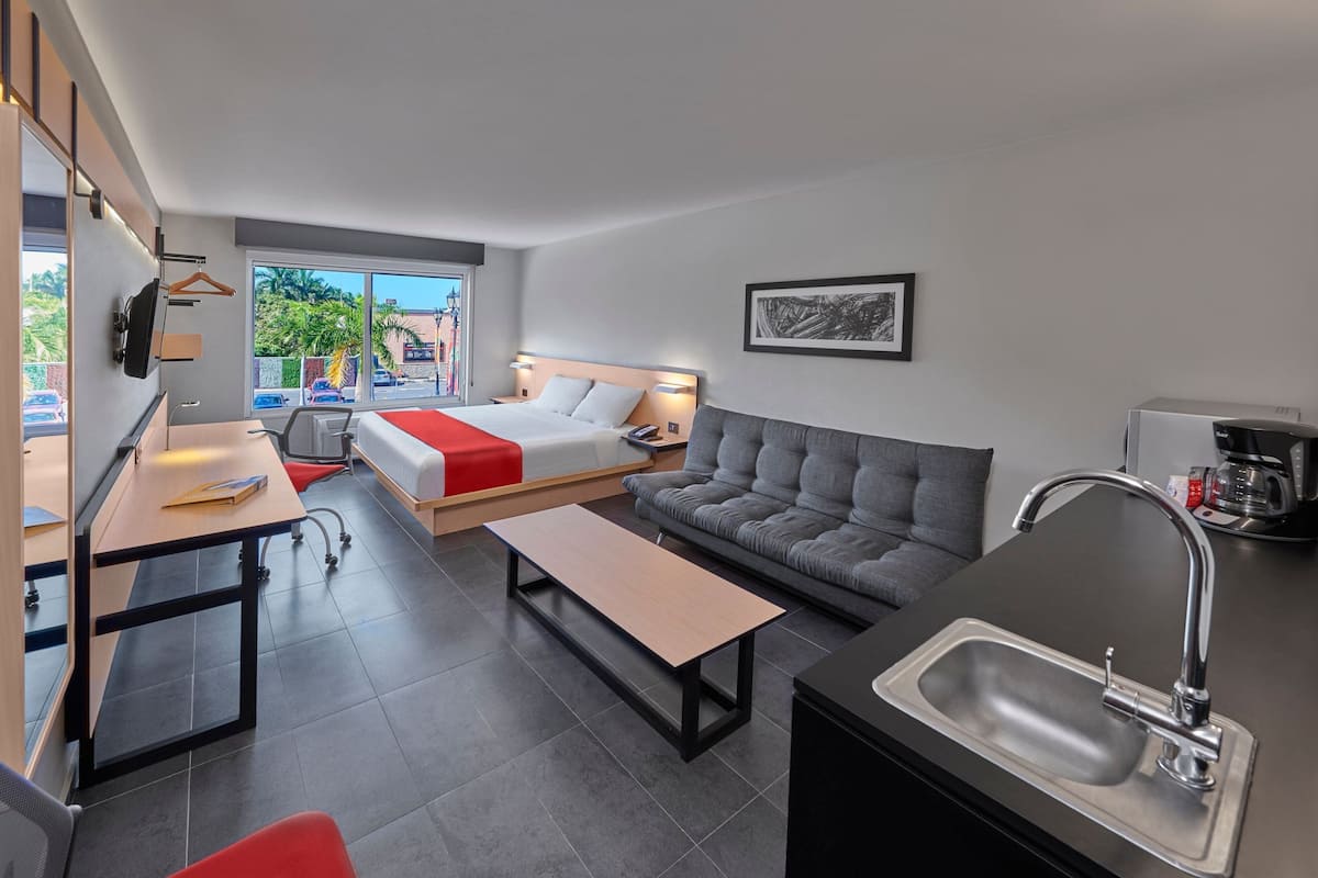 Una habitación de hotel moderna con cama, sofá, mesa de comedor y kitchenette.