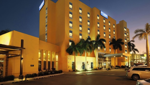 A multi-story hotel with a prominent 'City Express' sign, palm trees, and a parking area. - City Express by Marriott Tampico (Tampico)