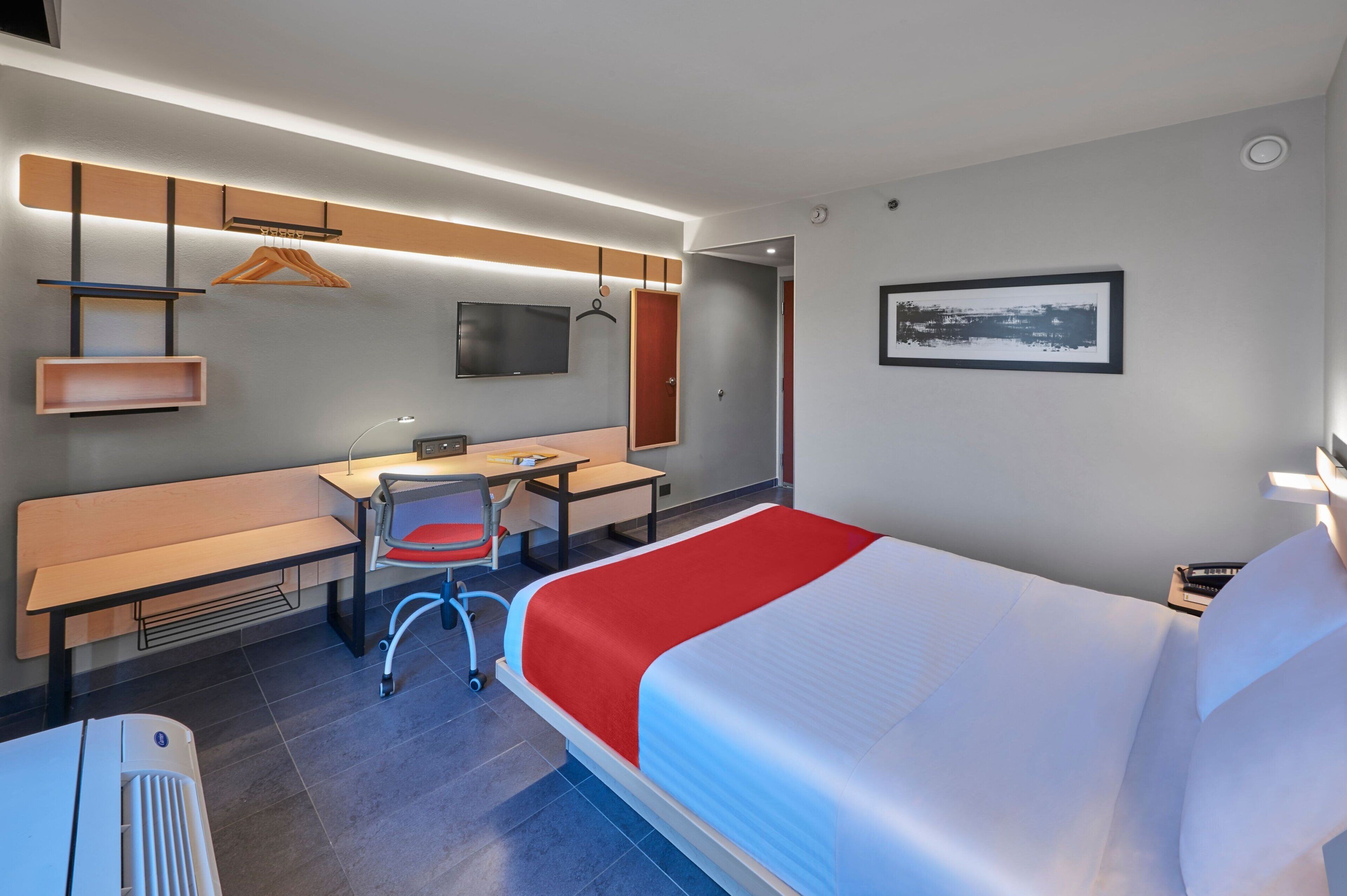 Een hotelkamer met een bed, bureau, stoel en een televisie aan de muur.