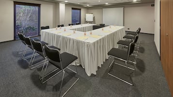 A conference room with a long table, black chairs, and a projector screen.