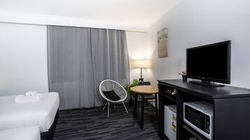 A hotel room with a bed, a desk with a computer, a television, and a microwave.