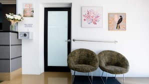 Uma área de recepção com porta de vidro, duas cadeiras com estampa de leopardo, um teclado de segurança e obras de arte na parede.