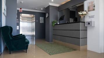 A reception area with a green velvet chair, a reception desk, a clock, and a fire panel sign.
