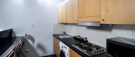 A modern kitchen with wooden cabinets, a stainless steel stove, a washing machine, and a microwave.