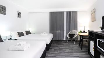 A hotel room with two beds, a desk, a chair, a TV, and a lamp.