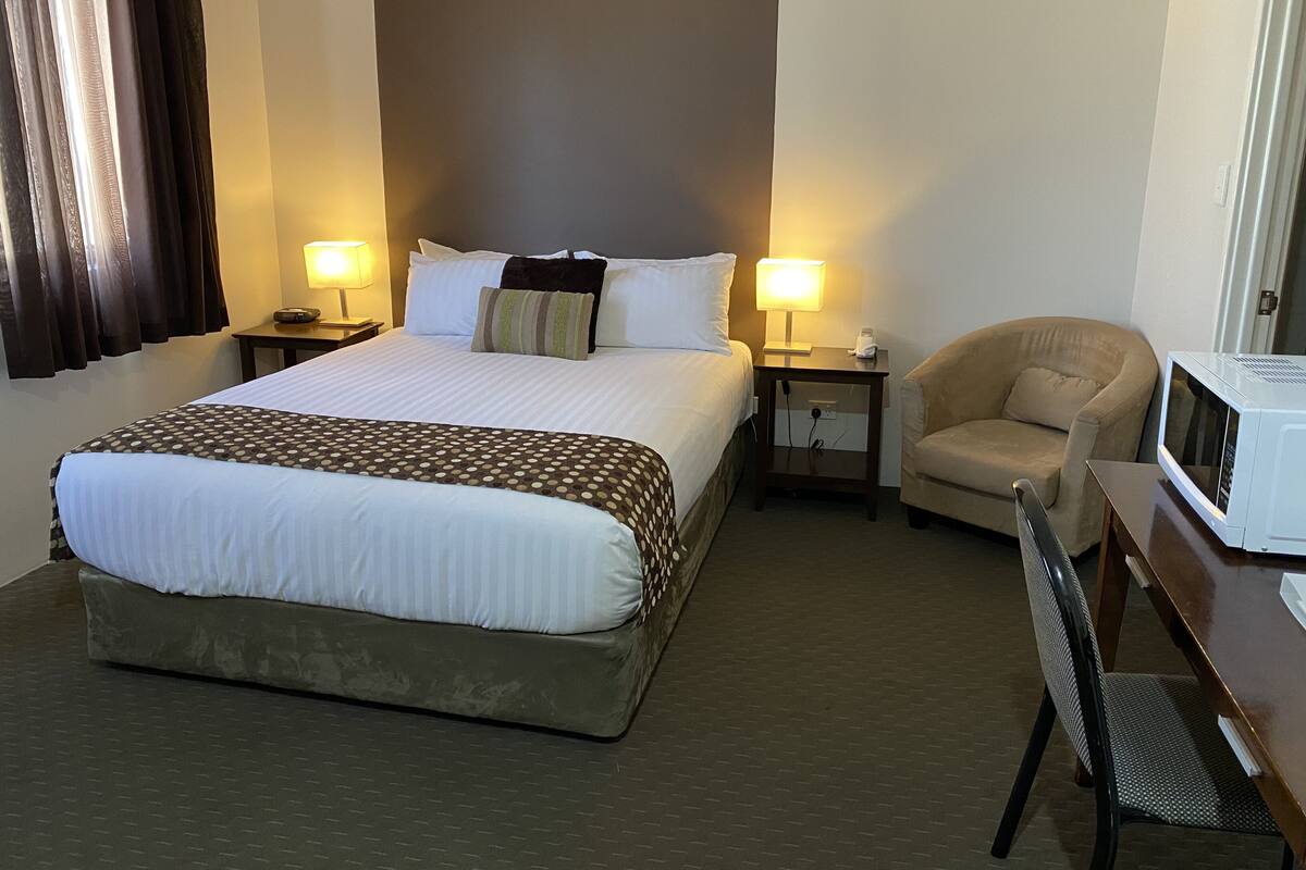 A hotel room with a large bed, two bedside tables with lamps, a chair, and a microwave.