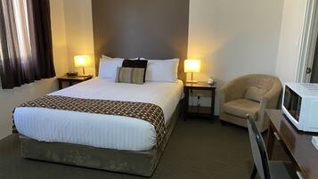 A hotel room with a large bed, two bedside tables with lamps, a chair, and a microwave.