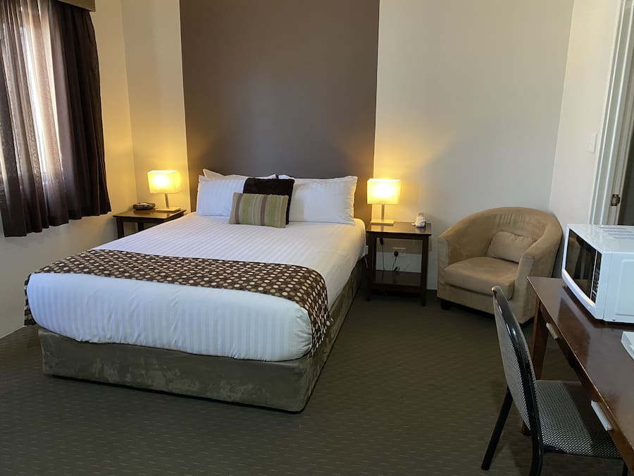 Ein Hotelzimmer mit einem großen Bett, zwei Nachttischen mit Lampen, einem Sessel und einer Mikrowelle.